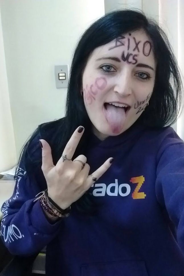 Jaqueline psicóloga com rosto pintado, fazendo sinal de "rock", expressando autenticidade e liberdade em sua identidade.