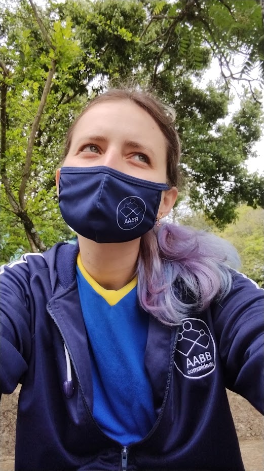 Jaqueline psicóloga de máscara azul, olhando para cima em meio à natureza, transmitindo serenidade e reflexão.