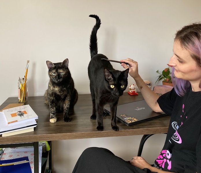 Jaqueline psicóloga sorrindo e trabalhando em sua mesa com seus gatos, transmitindo acolhimento na terapia online.